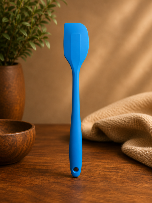 Blue spatula on a wooden surface with a plant and cloth in the background